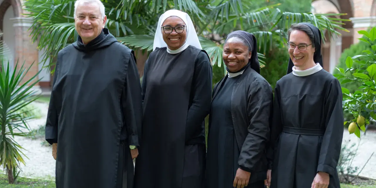 Four individuals in Benedictine habit smile in a garden.