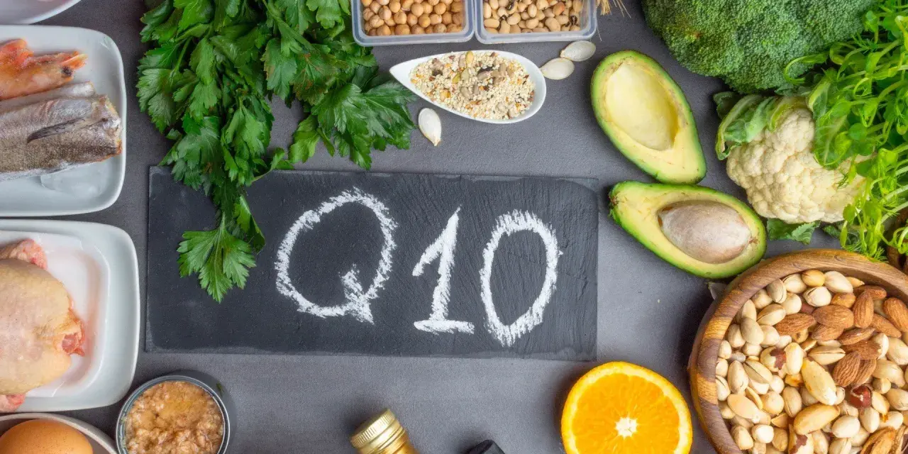 Q10 na tablicy, otoczone produktami bogatymi w koenzym Q10. Warto pamiętać o przeciwwskazaniach przy suplementacji.