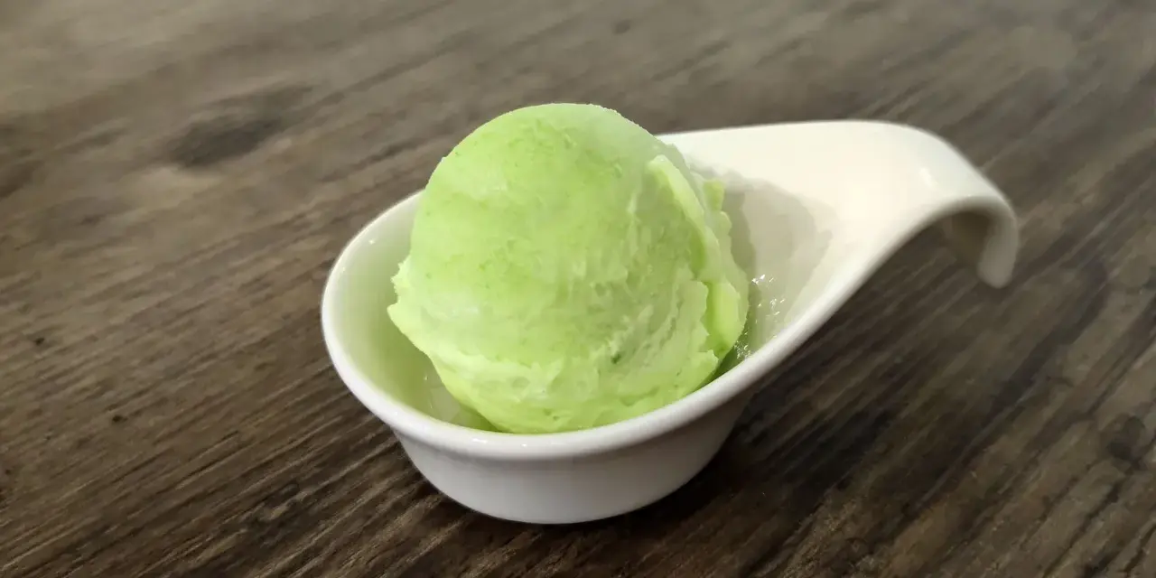 Una bola de helado de manzana verde brillante en una taza blanca sobre una mesa de madera.