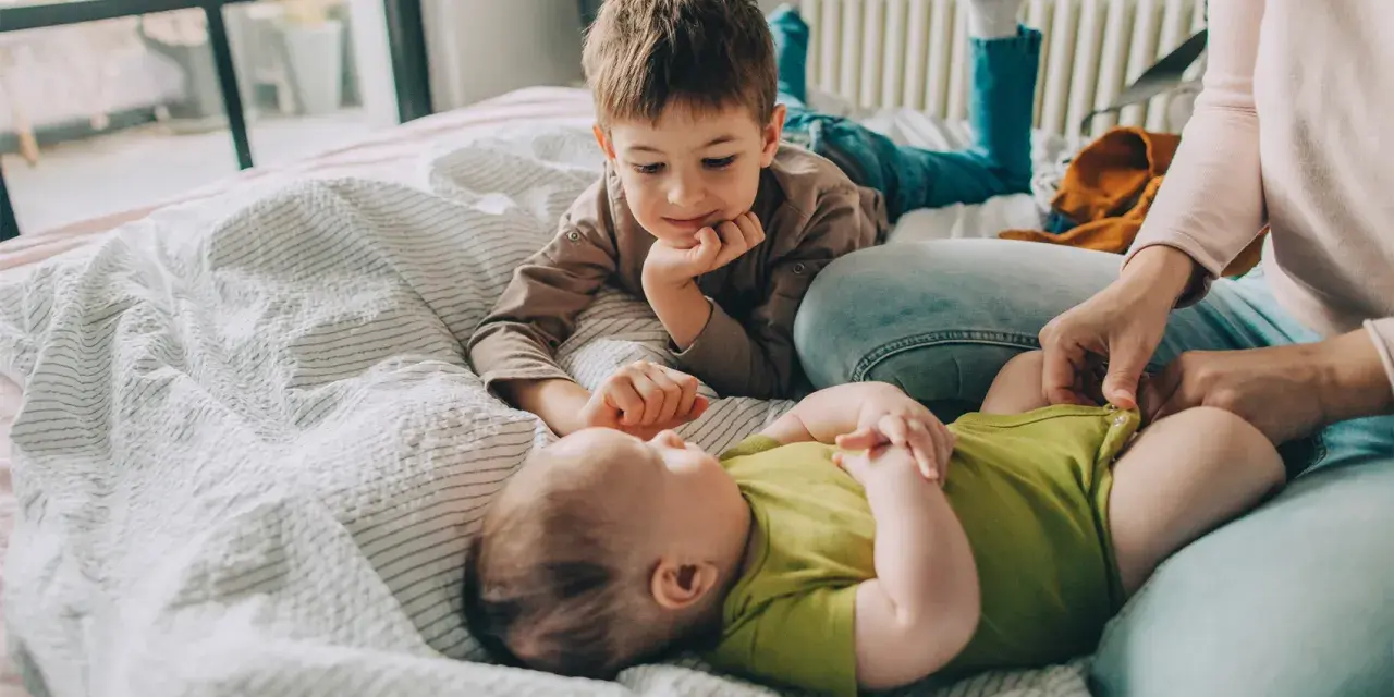 Starszy brat patrzy z czułością na niemowlę, zastanawiając się, ile niemowlę rośnie w miesiąc.
