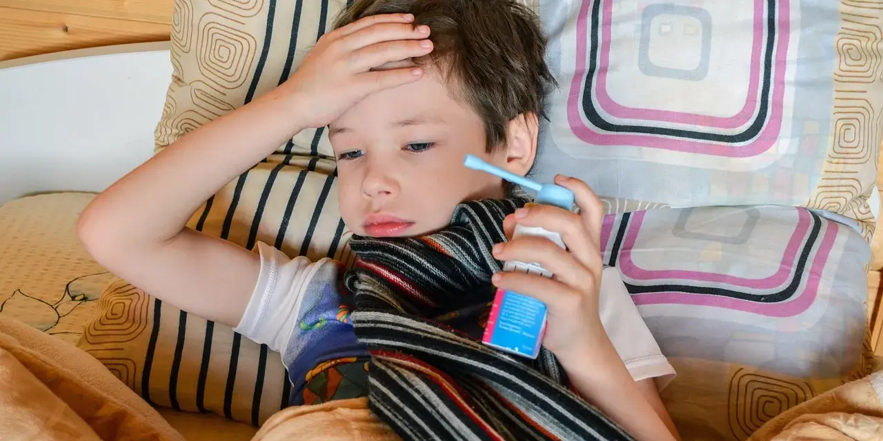 Chory chłopiec leży w łóżku z ręką na czole i trzyma inhalator.
