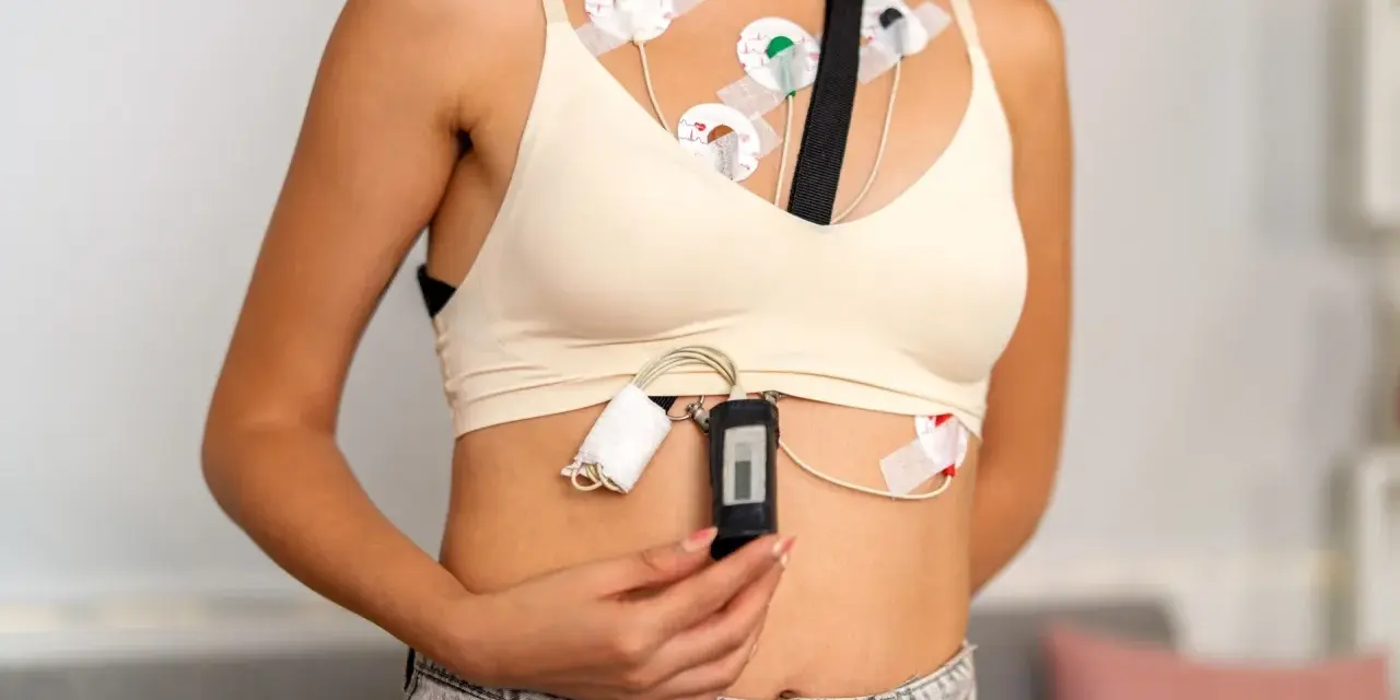 Kobieta z przyklejonymi elektrodami do klatki piersiowej, podłączonymi do rejestratora. To holter ekg, monitorujący pracę serca.