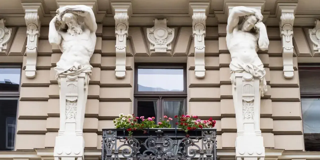 Dwie rzeźby atlantesów podtrzymujące balkon, przykład secesji w sztuce, zdobią fasadę kamienicy.