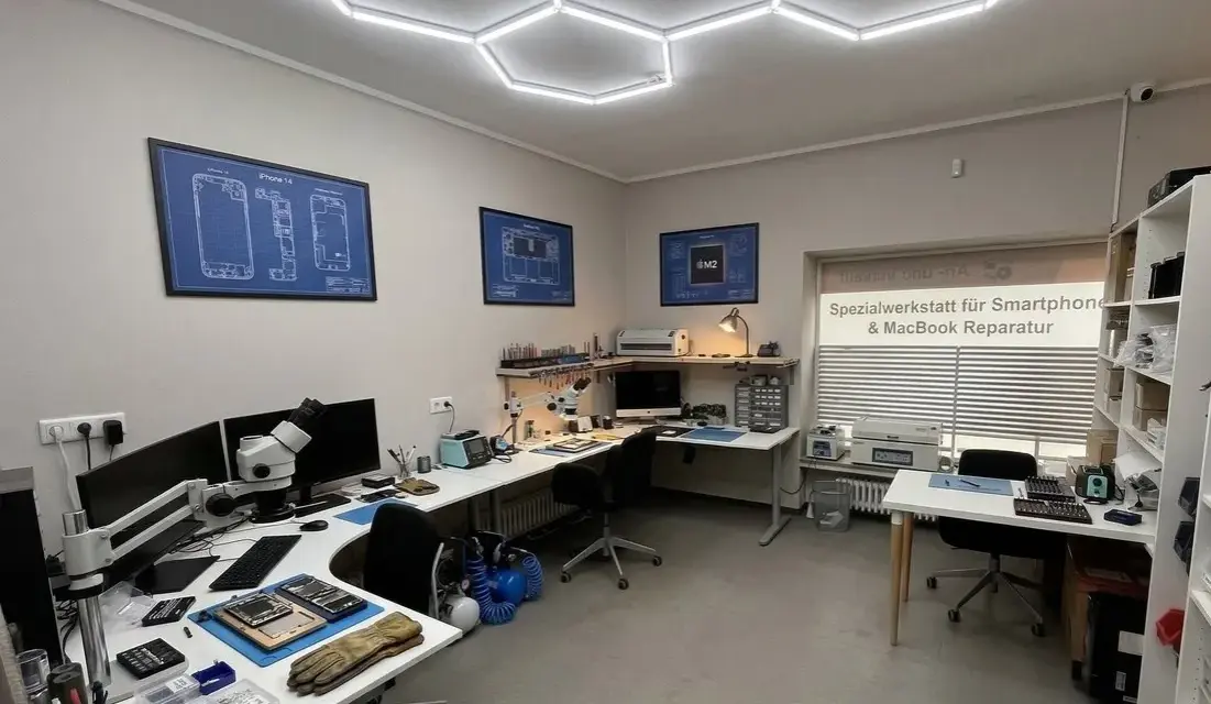 Werkstatt für Smartphone- und MacBook-Reparatur mit Werkzeugen, Mikroskop und technischen Zeichnungen.