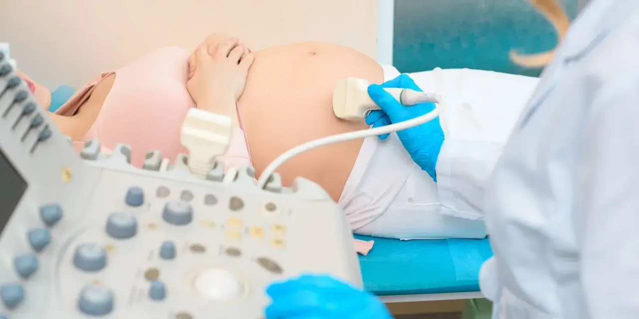 Badanie USG brzucha ciężarnej. Lekarz w niebieskich rękawiczkach wykonuje **test pappa**, sprawdzając stan płodu. Cena badania jest przystępna.