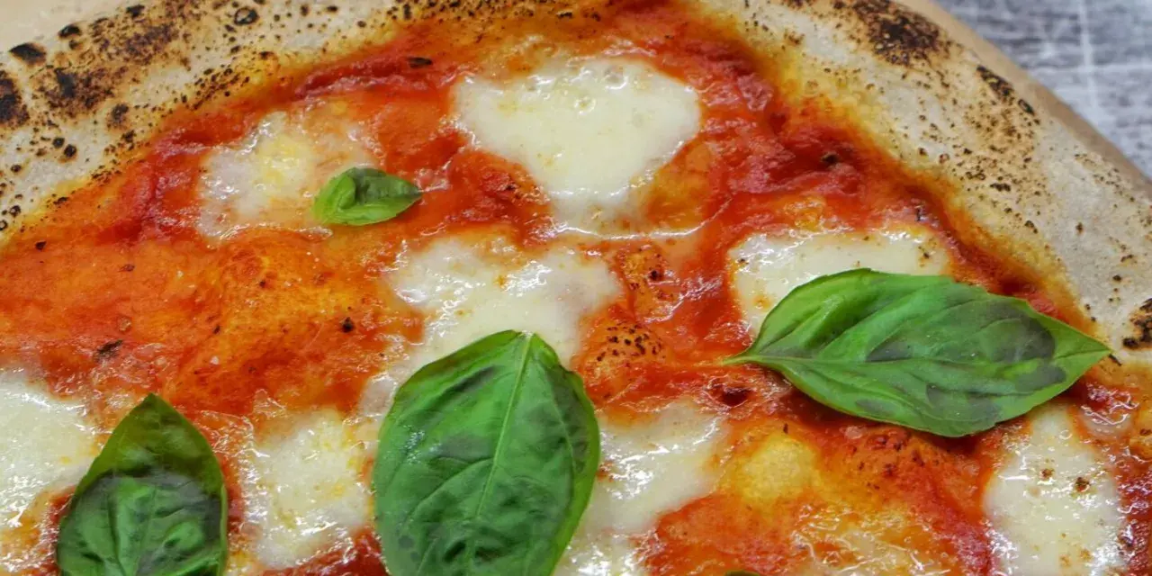 Ein Stück italienische Pizza Margherita mit geschmolzenem Mozzarella, Tomatensauce und frischem Basilikum. Perfekt für ein authentisches italien pizza rezept.