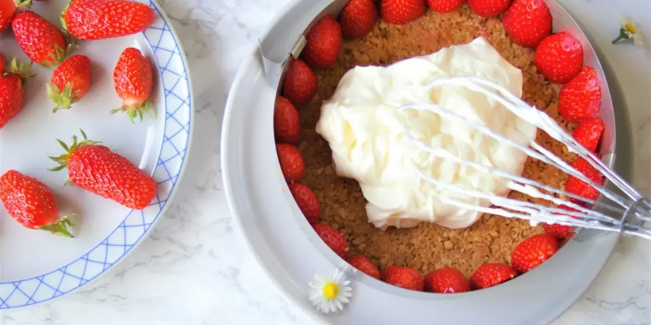 Préparation d'un cheesecake fraise : crème fouettée sur une base de biscuits et fraises fraîches.