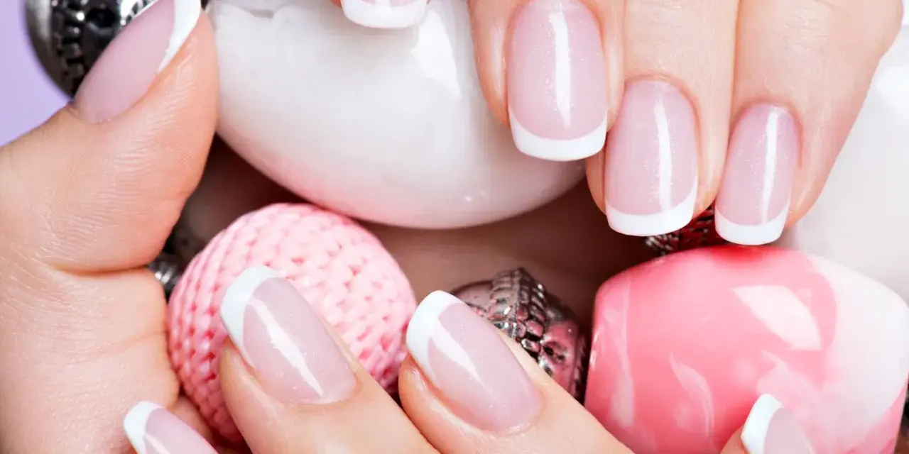 Dłonie z idealnym manicure francuskim, otoczone różowymi i białymi ozdobami.
