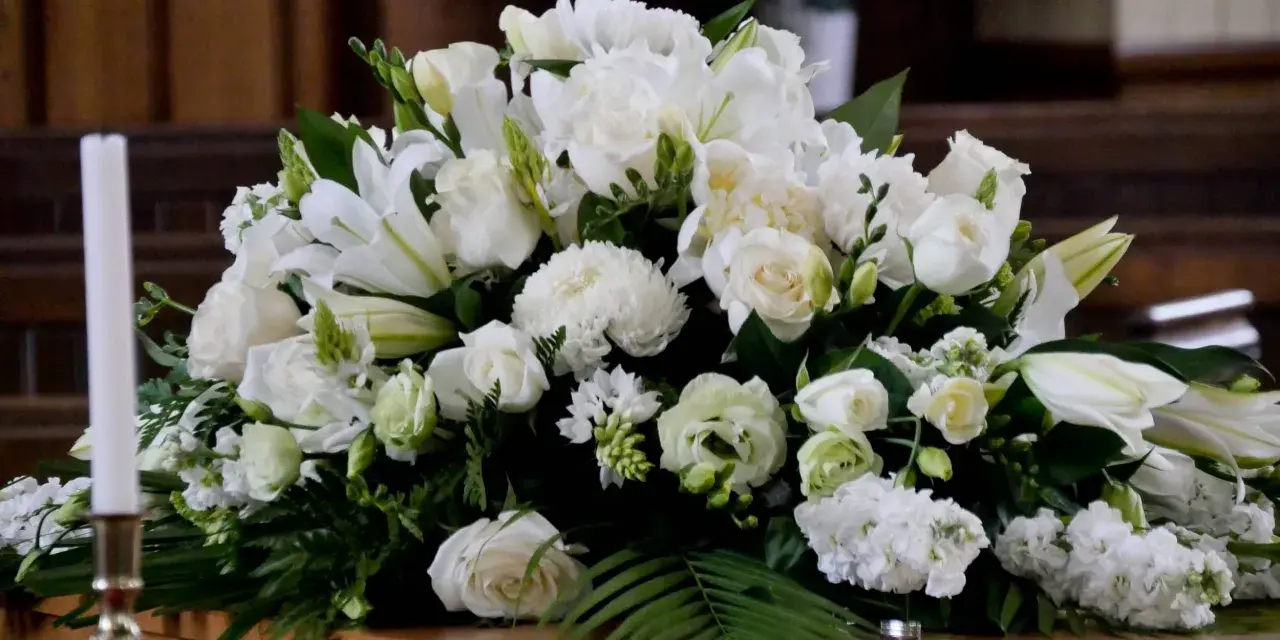 Un arreglo floral blanco sobre un ataúd, con lirios, rosas y otras flores. Estas flores para difuntos simbolizan paz y pureza en el adiós.