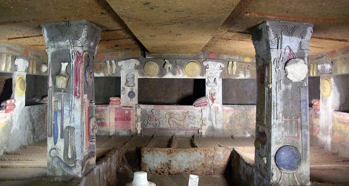 Inside a tomb at the Cerveteri Necropolis, painted columns and walls depict ancient life.