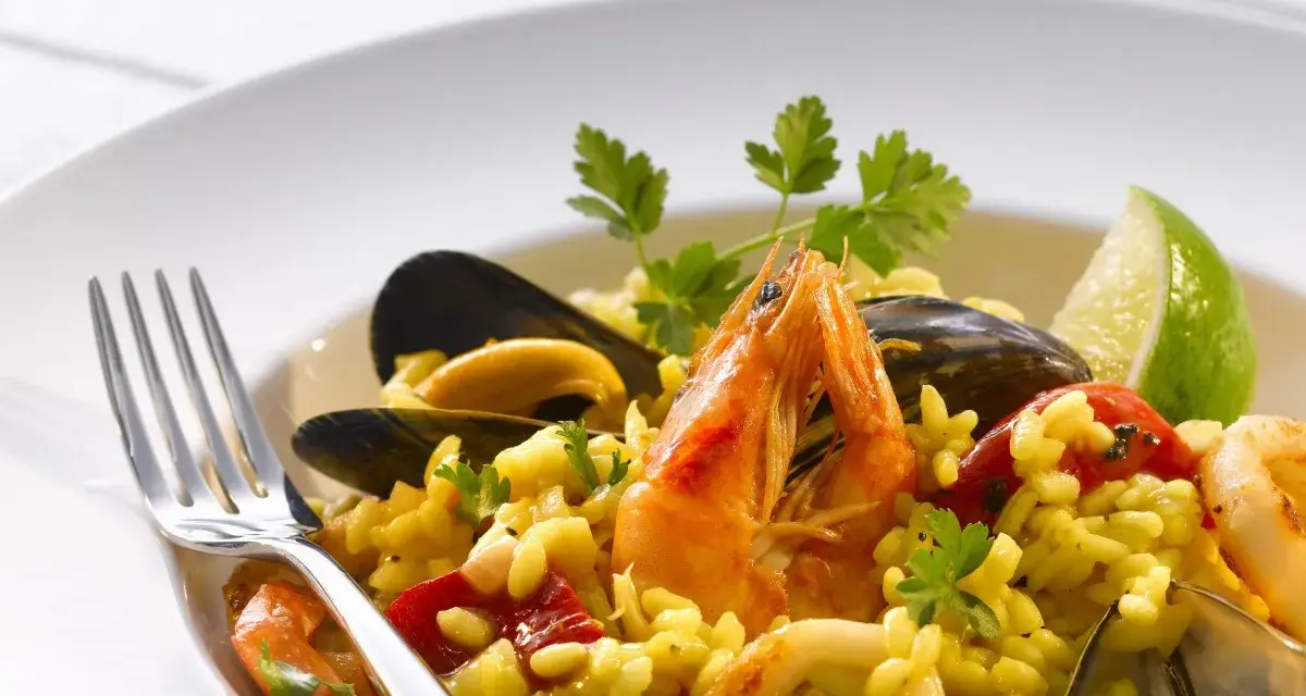 Pyszne risotto z owocami morza: krewetki, małże, kalmary i ryż, udekorowane natką pietruszki i ćwiartką limonki.