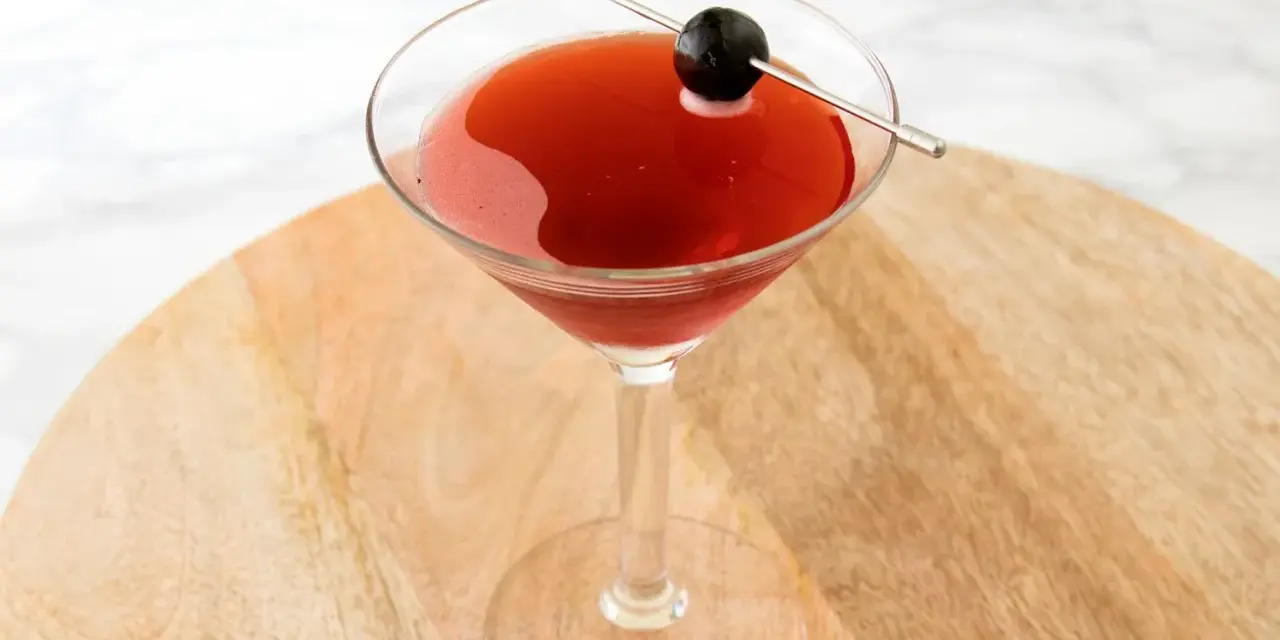 Czerwony drink w kieliszku koktajlowym, ozdobiony oliwką na wykałaczce. Idealny drink San Francisco na letnie wieczory.