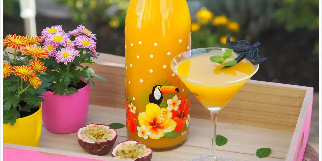 Tropische Früchte und ein leuchtend gelber Drink auf einer rosa Holzschale. Ein ideales Solero Schnaps Rezept ohne Sahne für heiße Tage.