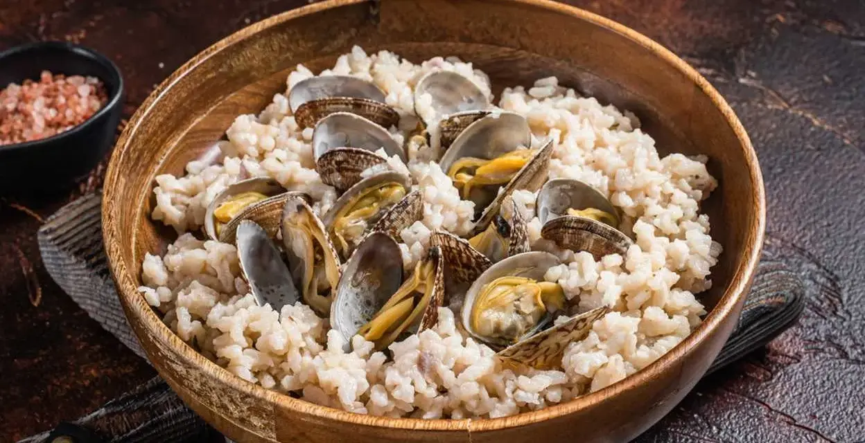 Un tazón de madera lleno de arroz cremoso y almejas frescas, un plato delicioso de arroz con almejas.