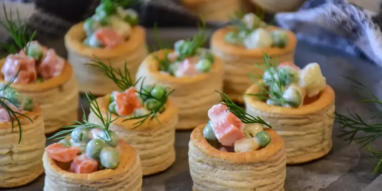 Petits bouchées à la reine, garnies d'une salade crémeuse de petits pois, carottes et jambon, décorées d'aneth. Parfaites pour un apéritif gourmand.