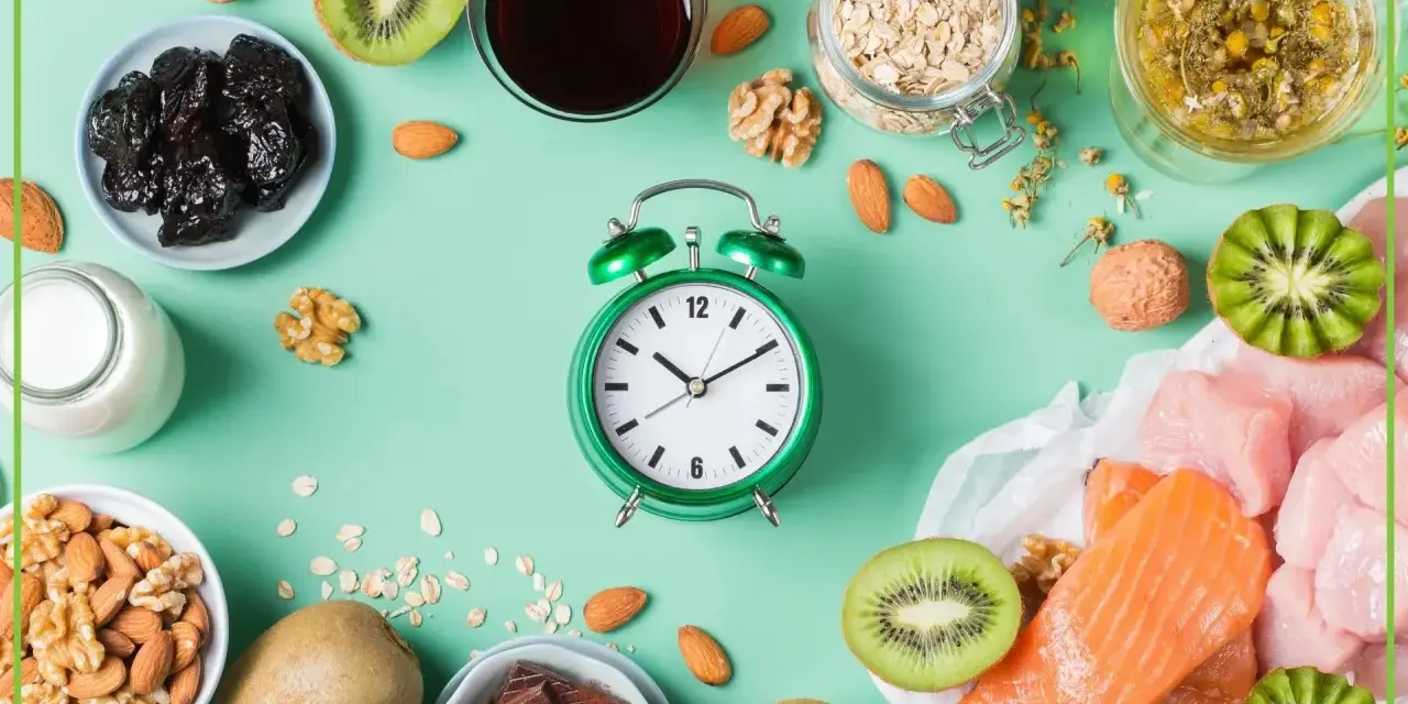 Zielony budzik obok produktów bogatych w tryptofan: łososia, indyka, kiwi, orzechów, migdałów, śliwek, mleka, owsa i czekolady. Zastanawiasz się, po jakim czasie działa tryptofan?