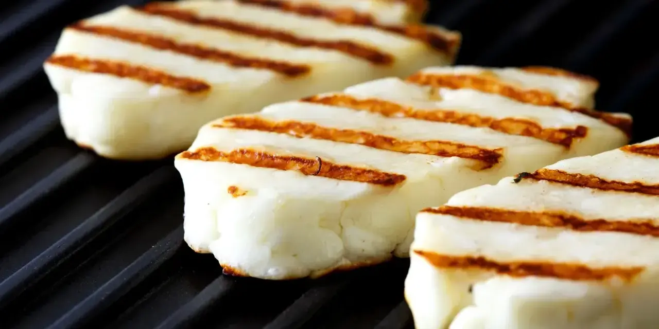 Trzy kawałki halloumi z grilla, z apetycznymi paskami, leżą na czarnej grillowej płycie.
