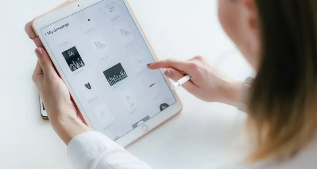 Kobieta tworzy rysowanie na iPadzie, przeglądając swoje prace. Stylus w dłoni sugeruje cyfrowe tworzenie.