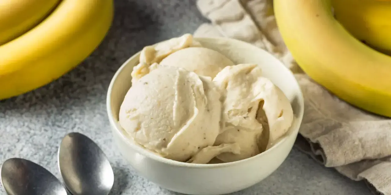 Un cremoso helado de plátano en un tazón blanco, con plátanos amarillos frescos al lado.