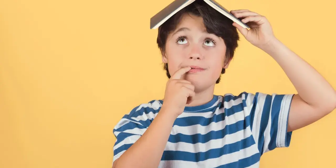 Un enfant de 5 ans, avec un livre sur la tête, réfléchit. Il est en colonie de vacances.