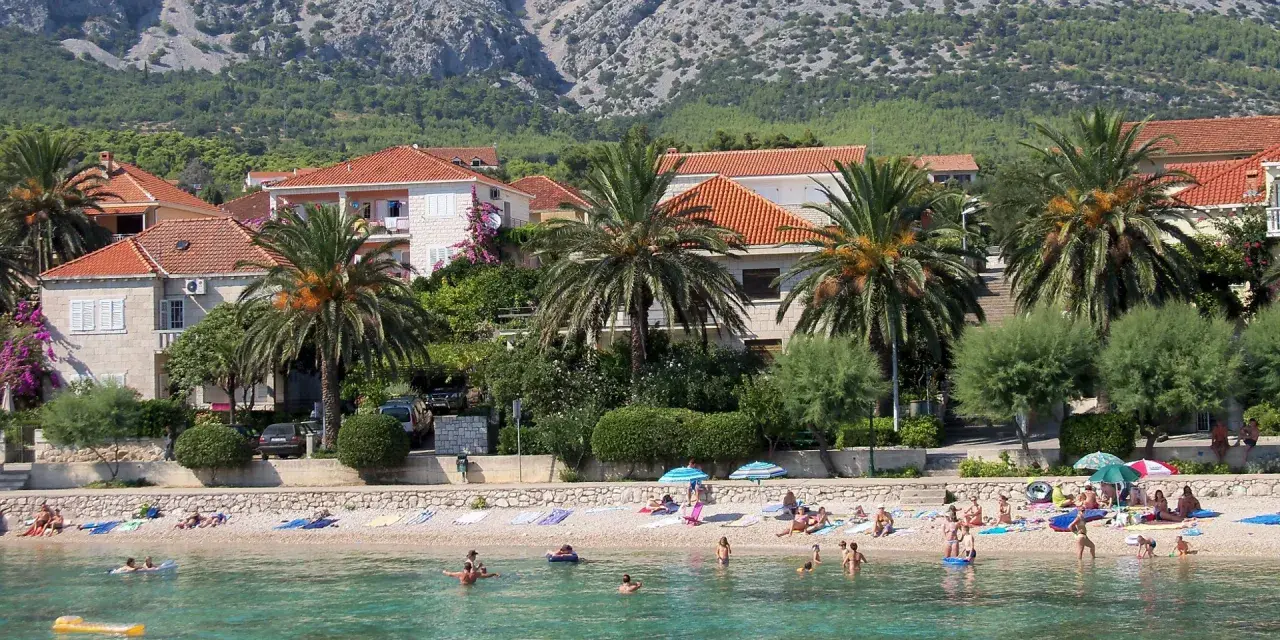 Plaża z palmami, domami i ludźmi kąpiącymi się w morzu.