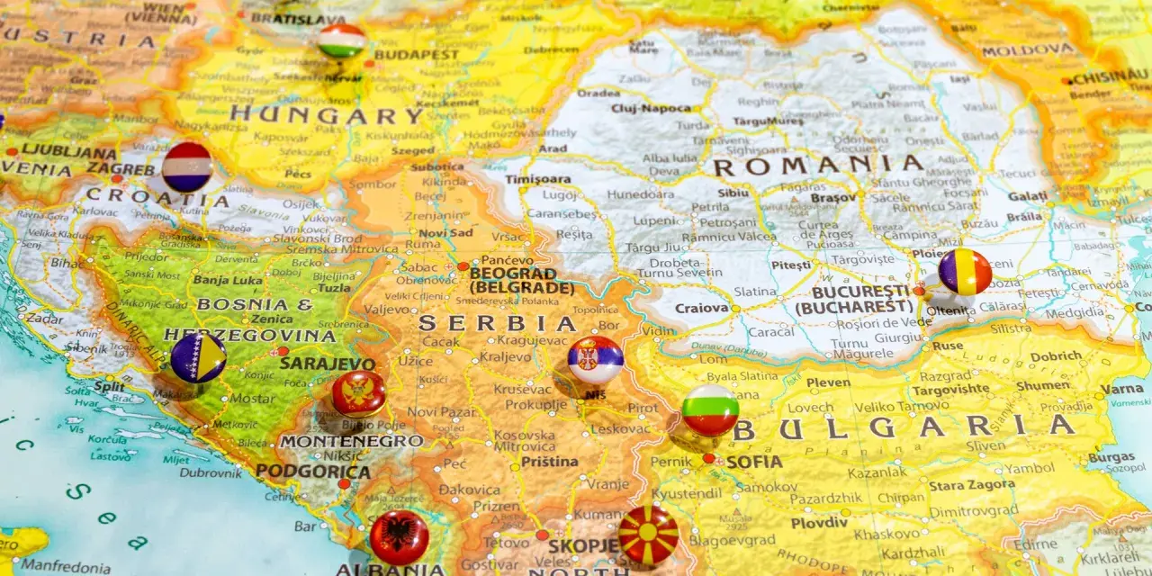 Mapa Europy z zaznaczonymi krajami bałkańskimi, w tym Serbią, Bułgarią i Rumunią, z flagami narodowymi w miejscach stolic.