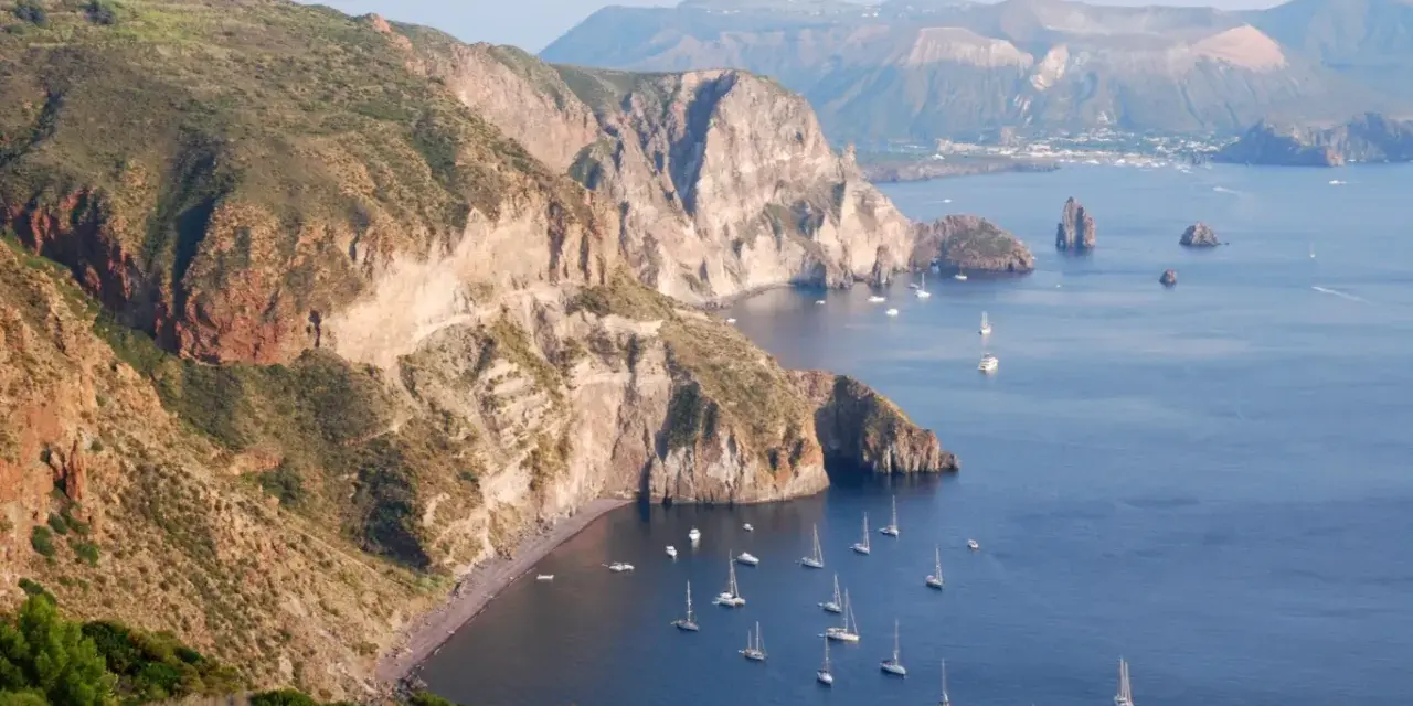 Malownicze wyspy liparyjskie z klifami, zatoczkami i licznymi żaglówkami na lazurowym morzu.