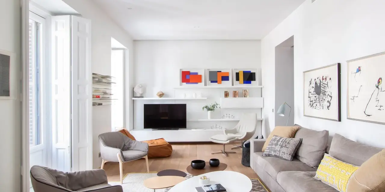 Salón moderno con sofás grises, mesas de centro y arte abstracto. Se aprecia la sutil diferencia entre blanco y blanco roto en paredes y carpintería.