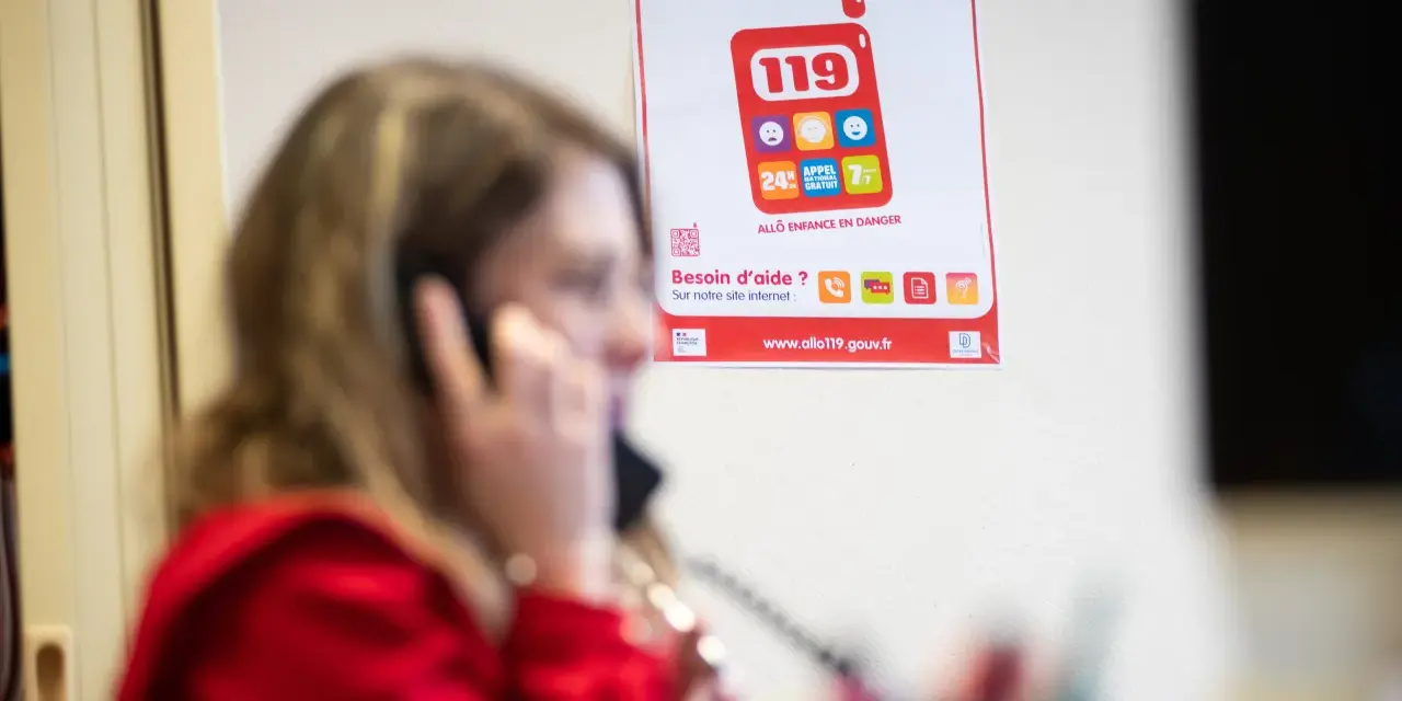 Une femme au téléphone, devant une affiche expliquant le crip signification du numéro 119 pour les enfants en danger.