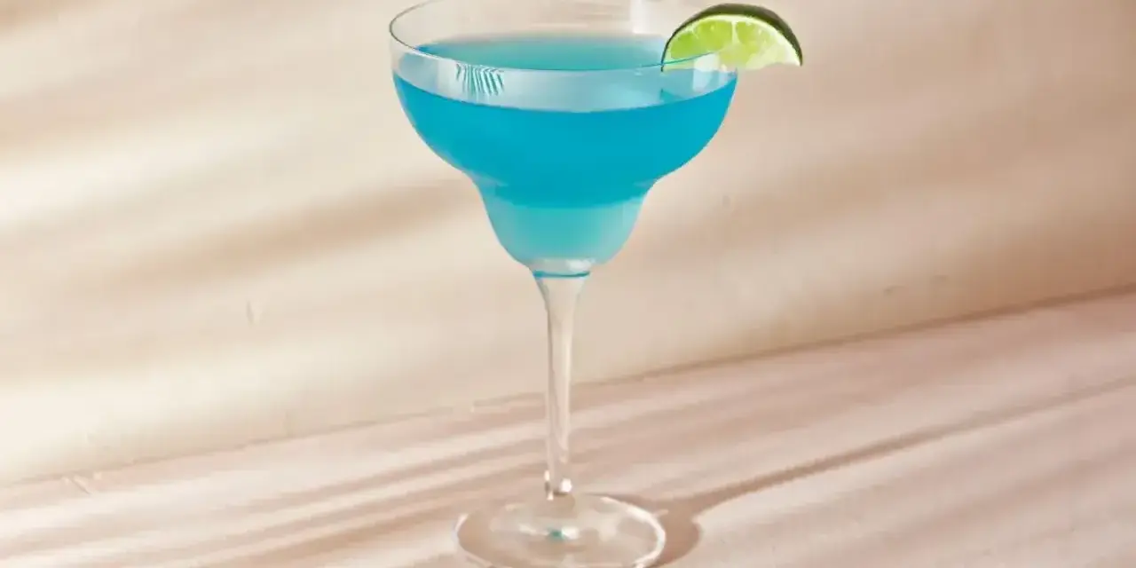 Niebieski drink z ginem, tonikiem i blue curacao, ozdobiony plasterkiem limonki, wygląda orzeźwiająco.