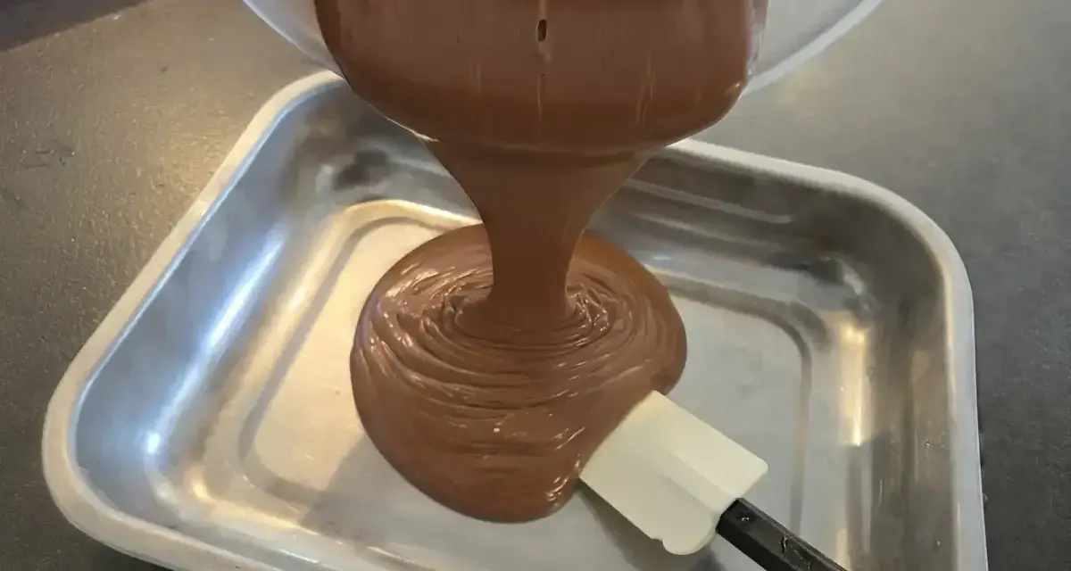 Comment faire une ganache : du chocolat fondu coule d'un bol dans un plat, guidé par une spatule.