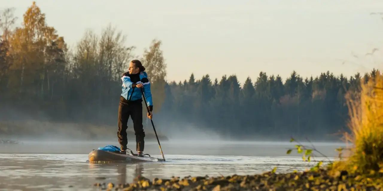 Mann auf Stand Up Paddle, achtet auf die ruhige Wasseroberfläche und die neblige Morgenstimmung.