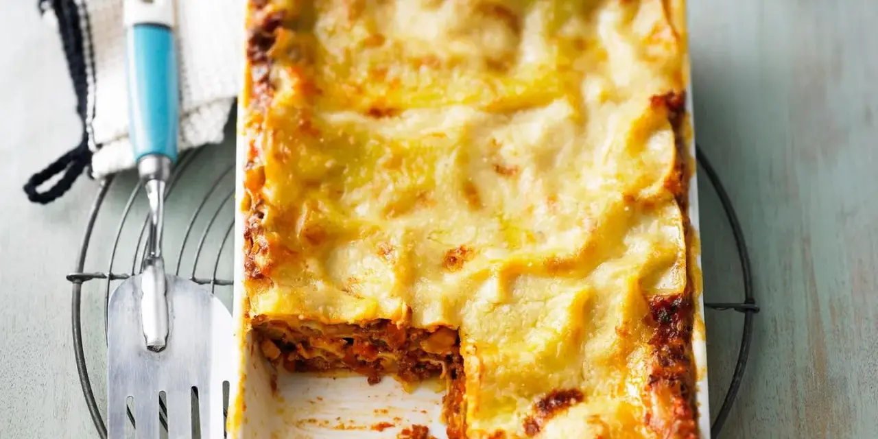 Eine frisch gebackene, italienische Lasagne in einer Auflaufform, mit einer goldbraunen Käseschicht und einem Stück herausgenommen.