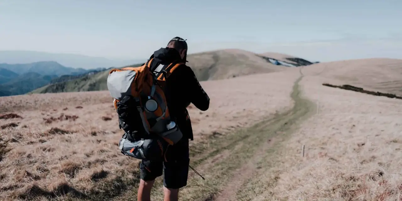 Uomo con zaino da trekking su un sentiero di montagna.