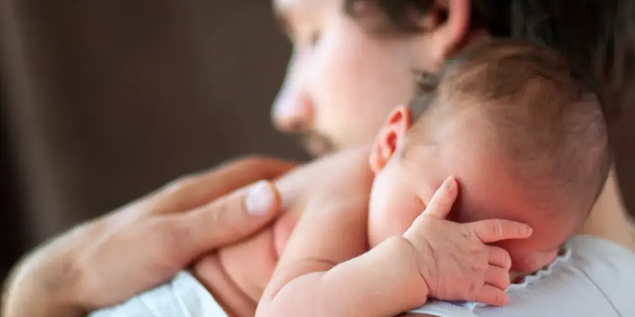 Padre abbraccia neonato. Osservare attentamente i sintomi autismo nel neonato di 3 mesi, come la mancanza di contatto visivo o risposte emotive atipiche.