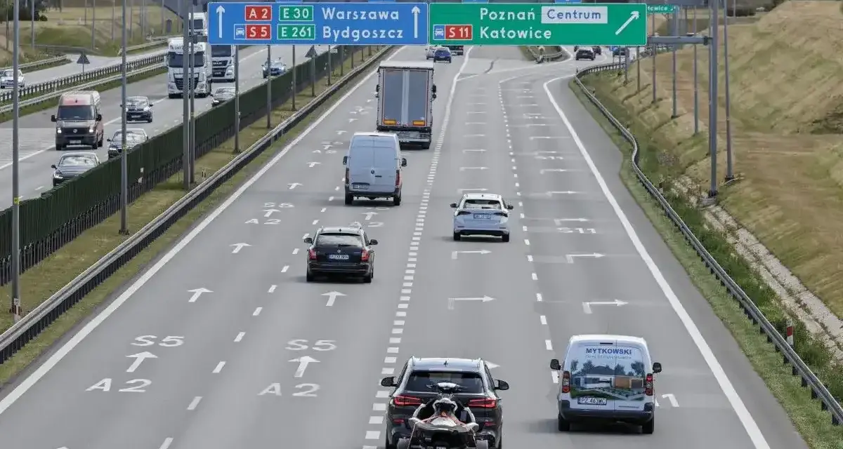 Autostrada z ruchem samochodów, znakami drogowymi kierującymi do Warszawy, Bydgoszczy, Poznania i Katowic.