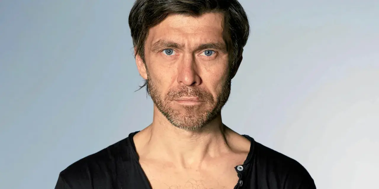 Marcin Czarnik, aktor o intensywnym spojrzeniu i niebieskich oczach, w czarnej koszulce.