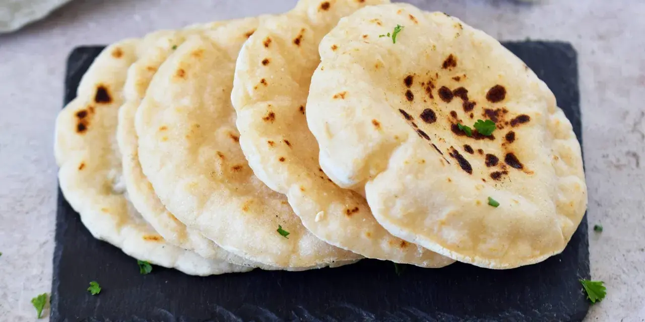 Frisch gebackenes pita brot, leicht gebräunt und mit Petersilie garniert, liegt auf einem dunklen Stein.
