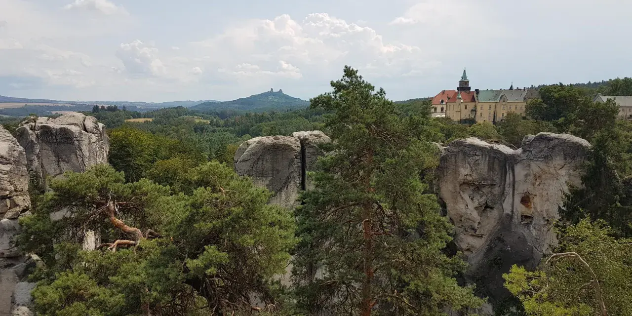 Widok na zamek Hrubá Skála otoczony skalnymi formacjami i lasem.