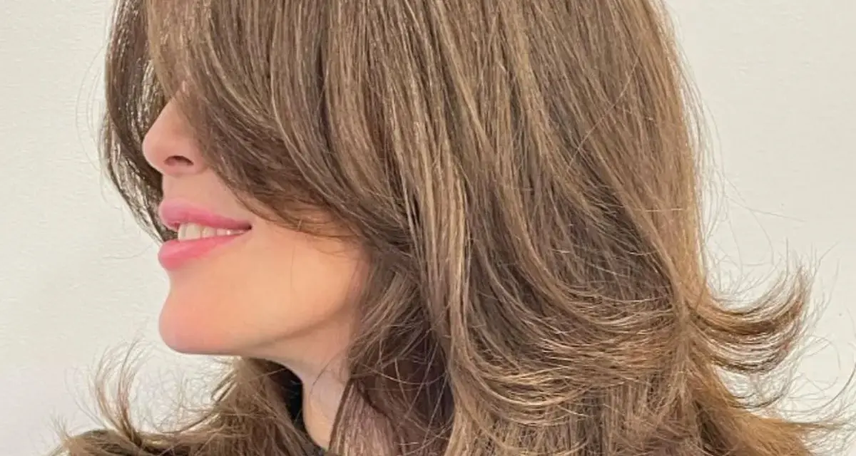 Mujer sonríe con un corte mariposa pelo largo, con capas que enmarcan su rostro.