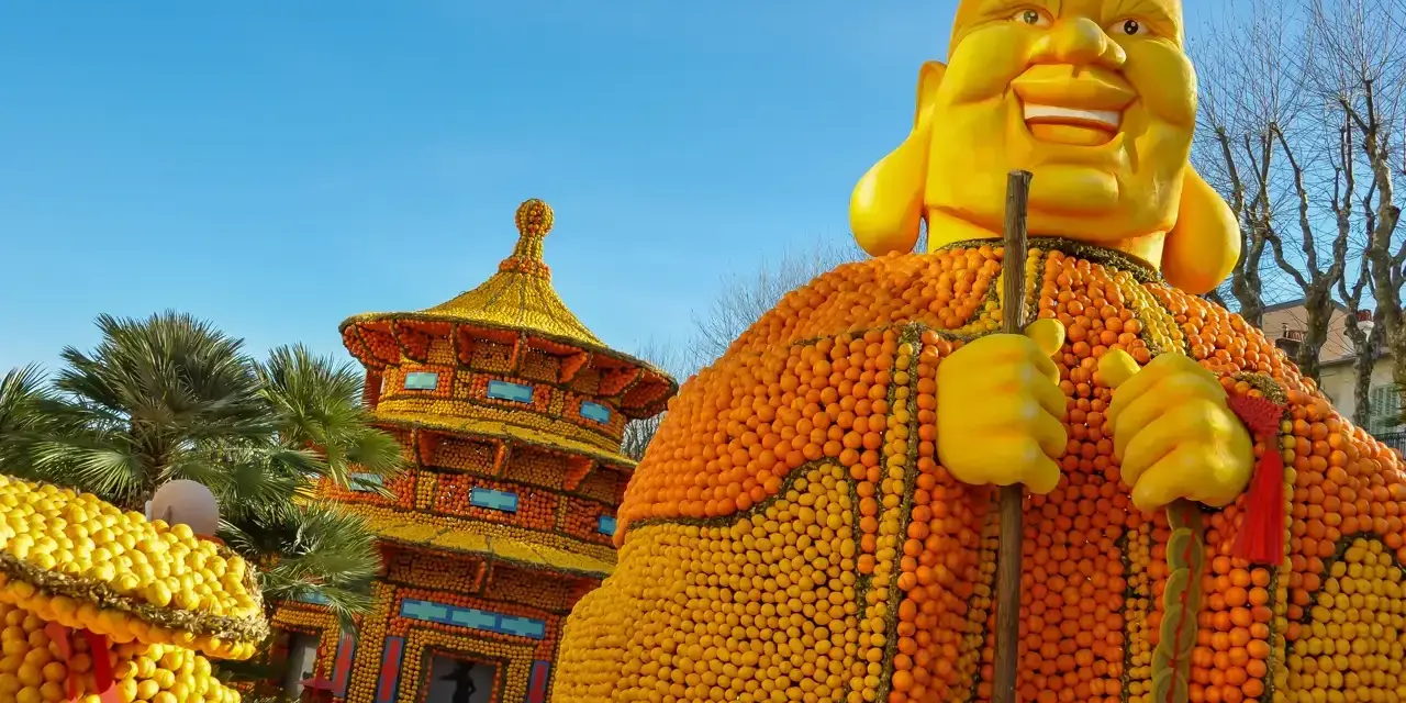 Escultura gigante de Buda hecha de naranjas y limones, parte del menton lemon festival, con una pagoda de frutas al fondo.