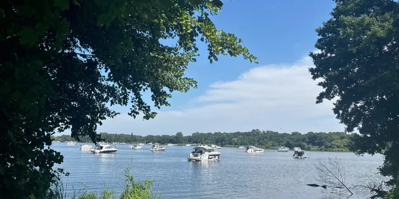 Boote auf dem Glindower See unter blauem Himmel, umgeben von grünen Bäumen. Ein sonniger Tag am Wasser.