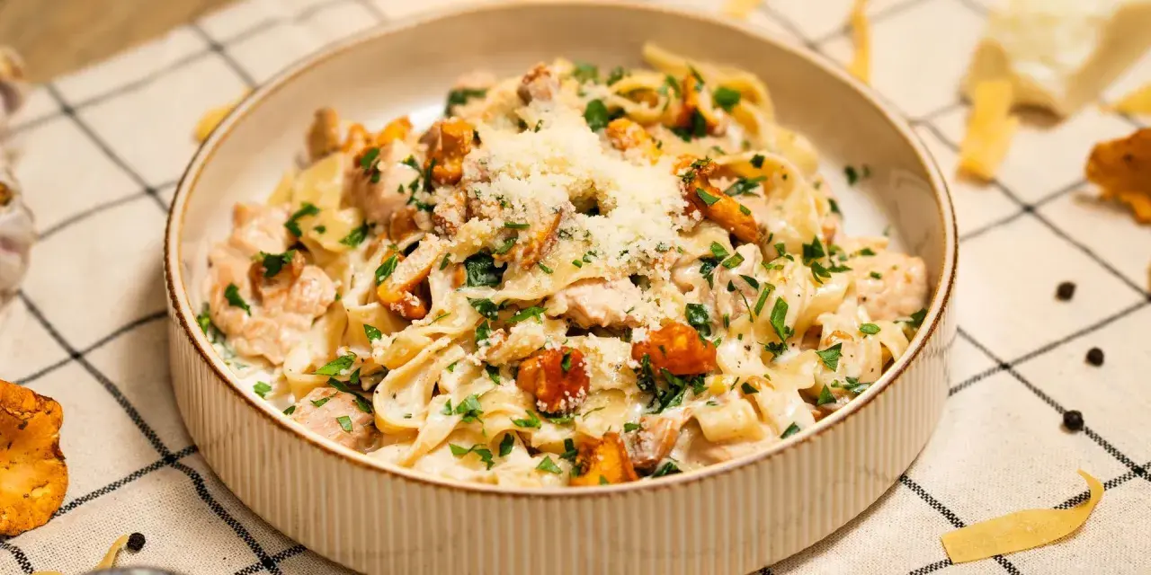 Pyszny makaron w sosie kurkowym z kawałkami kurczaka i posypany parmezanem.