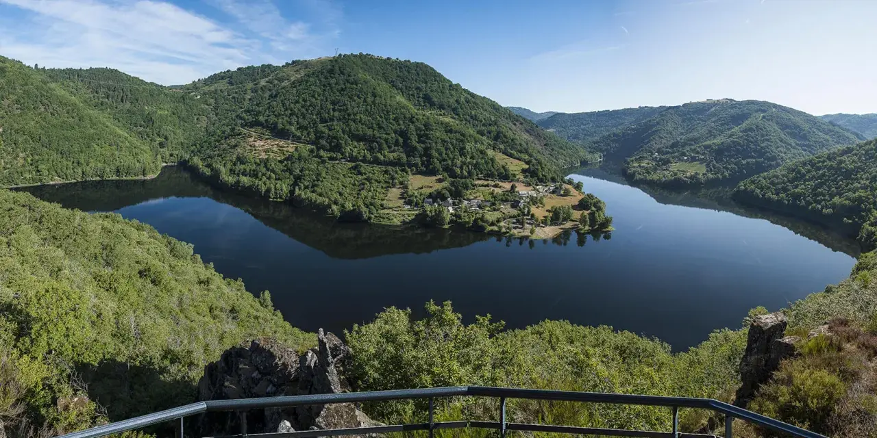 Vue panoramique des gorges de la Truyère, un lac paisible reflétant les collines verdoyantes. Idéal pour la randonnée.