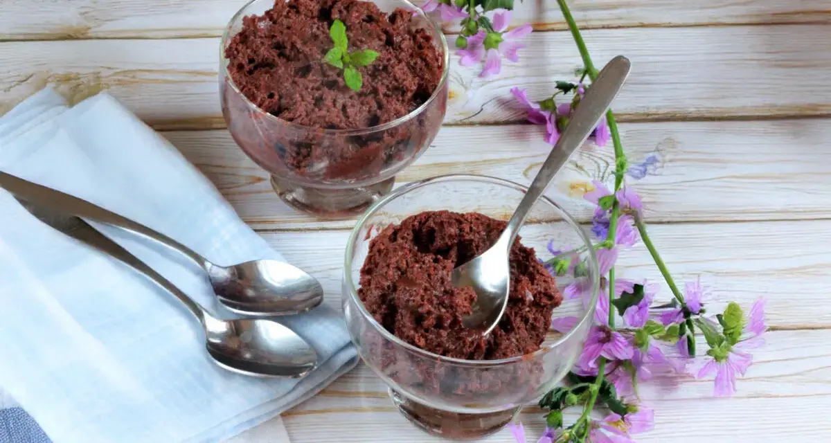 Dos copas de delicioso mousse de chocolate de la abuela, decoradas con menta y flores moradas, listas para disfrutar.