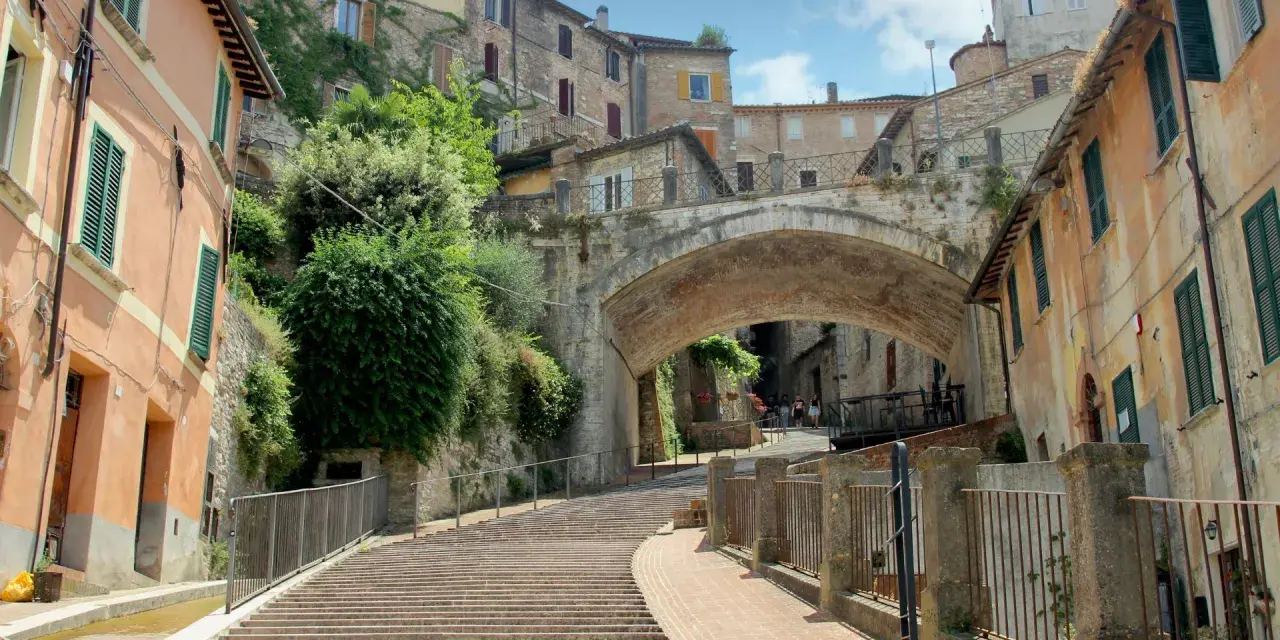 Perugia co zobaczyć: malownicze schody prowadzące pod zabytkowy most, otoczone kamiennymi domami i zielenią.