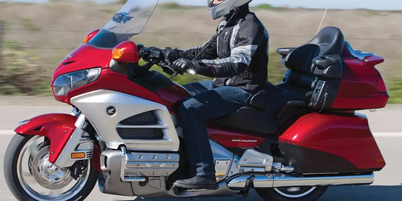 Mężczyzna w kasku jedzie lśniącym, czerwonym motocyklem turystycznym Honda Gold Wing.