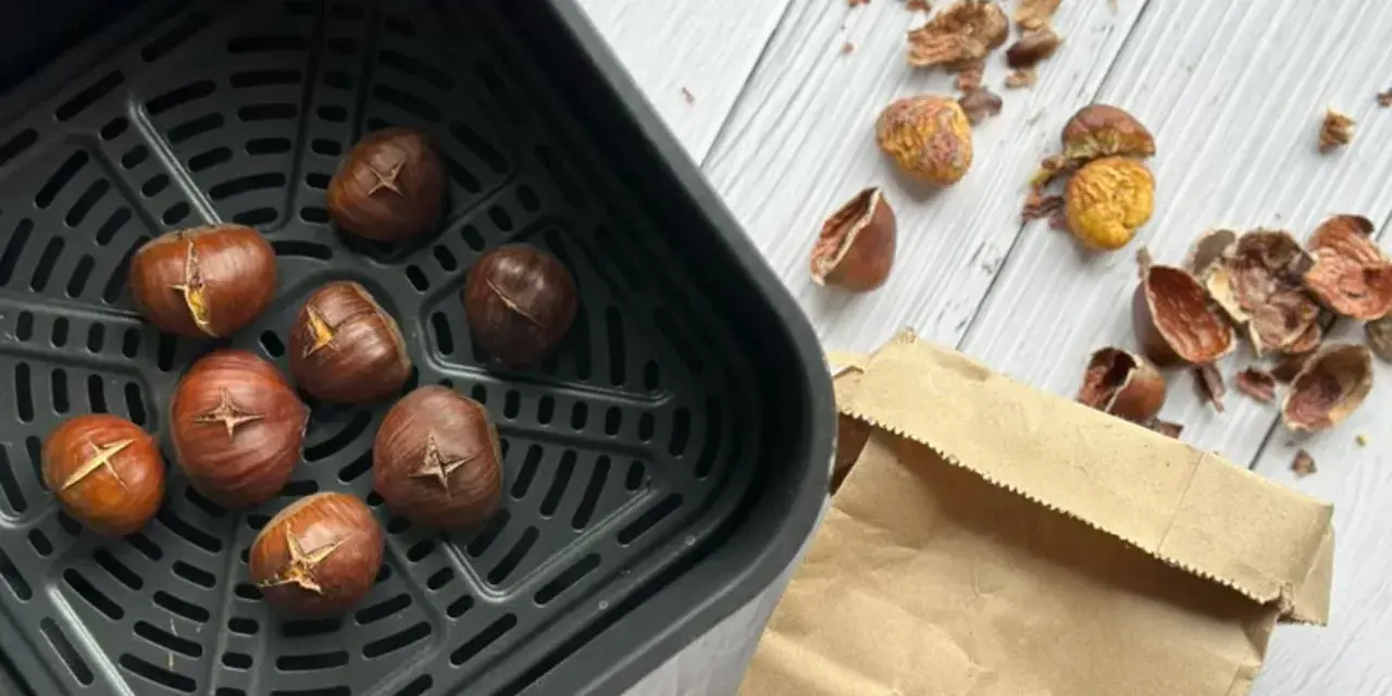 Châtaignes grillées dans le panier de l'air fryer, prêtes à être dégustées. Les écorces vides jonchent la table.