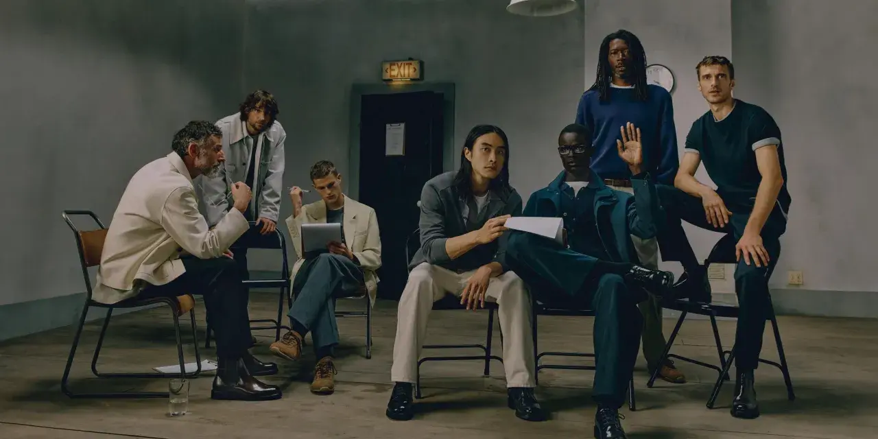 Grupo de hombres con un look business casual, sentados y de pie en una sala con un letrero de "EXIT".