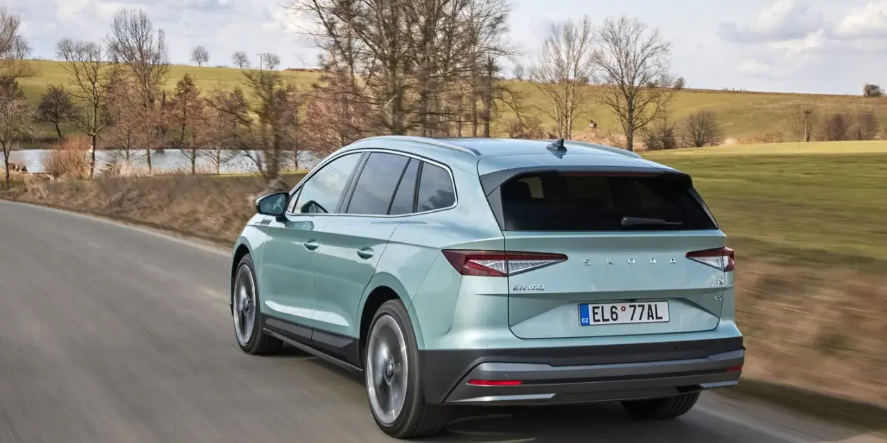 Jasnozielony Skoda Enyaq jedzie po wiejskiej drodze, otoczony wiosennym krajobrazem z drzewami i zielonymi polami.
